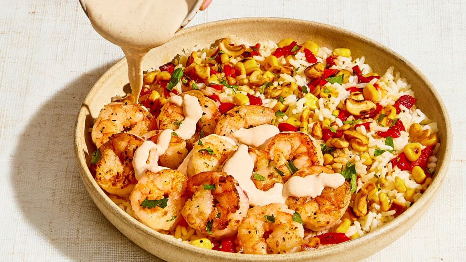 Sauce being poured over a bowl of shrimp with rice, corn and peppers
